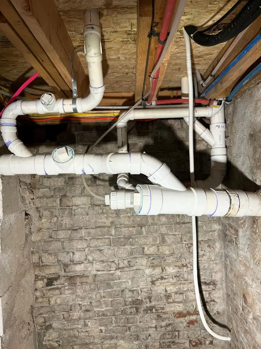 White PVC drain and vent piping under the floor of a Somerville remodel